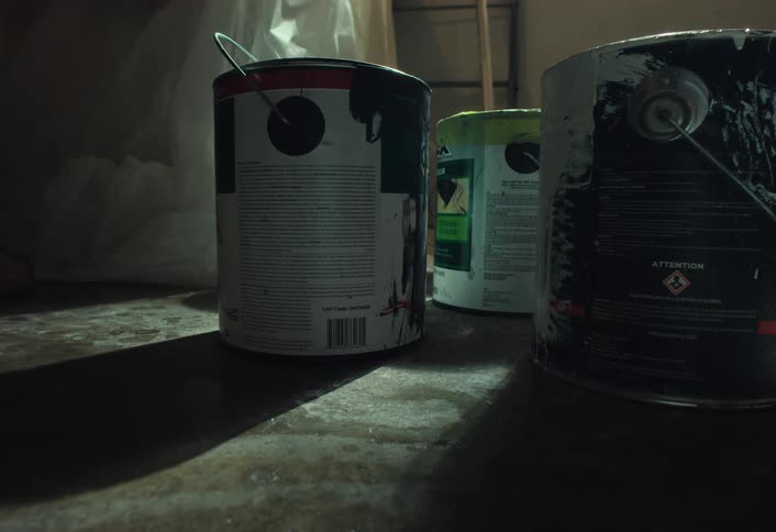 A messy paint can is placed on a dirty concrete floor in a dimly lit, unfinished room