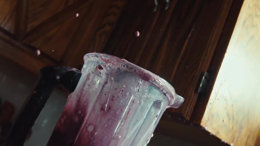 A close-up, low-angle shot captures a messy berry smoothie exploding from a blender in dramatic slow motion