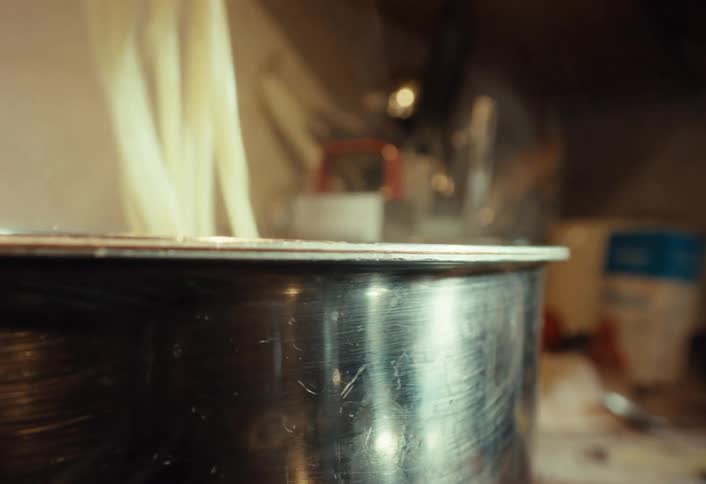 Close up shot of stirring and lifting hot steaming pasta from a stainless steel pot