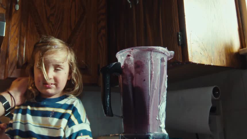 A father comforts his young son as a purple smoothie explodes out of a blender in super slow motion, making a huge mess in the kitchen