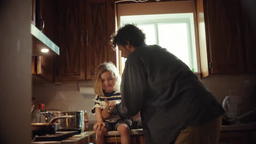 A mischievous little boy pours a pot of spaghetti on his father's head, leading to a playful and messy scene in the kitchen