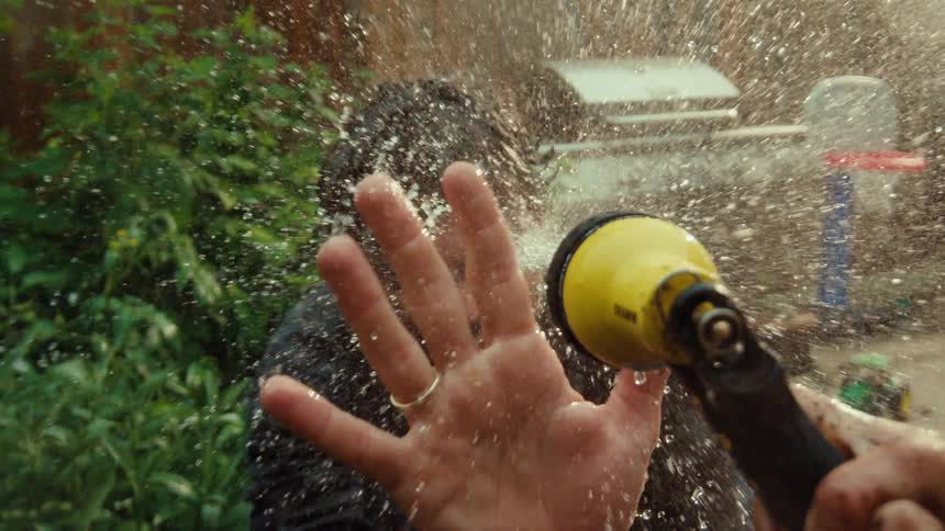 A man laughs while being sprayed in the face with a garden hose in a playful moment captured in super slow motion
