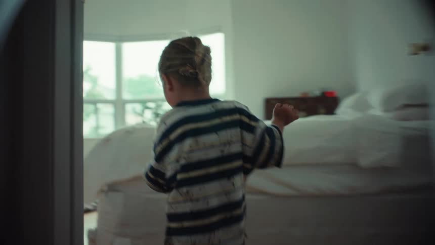 A slow-motion shot follows a mischievous young boy covered in mud as he runs barefoot through a dimly lit hallway into a bedroom
