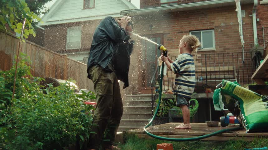 A little girl playfully sprays her father with a water hose in their backyard in slow motion