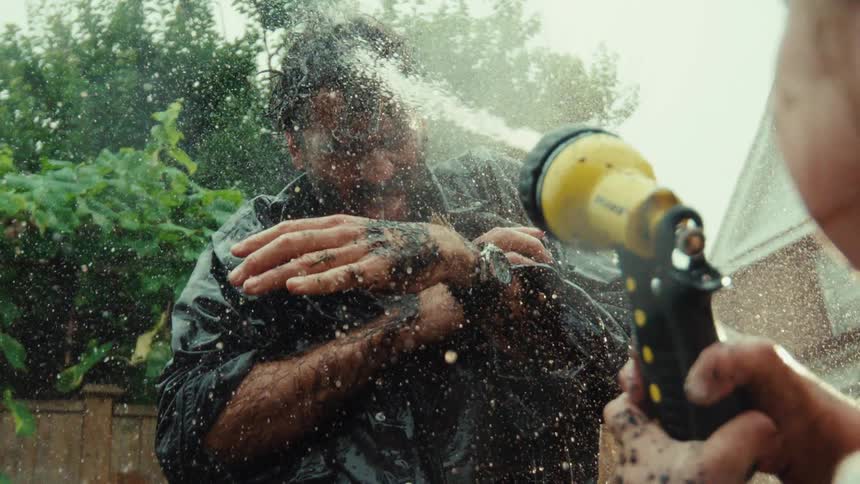 Super slow motion close-up of a dirty man getting sprayed in the face with a garden hose