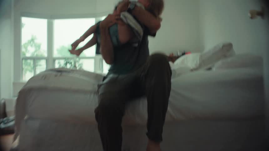 A low-angle perspective follows muddy footprints into a bedroom where a father playfully wrestles his child on the bed