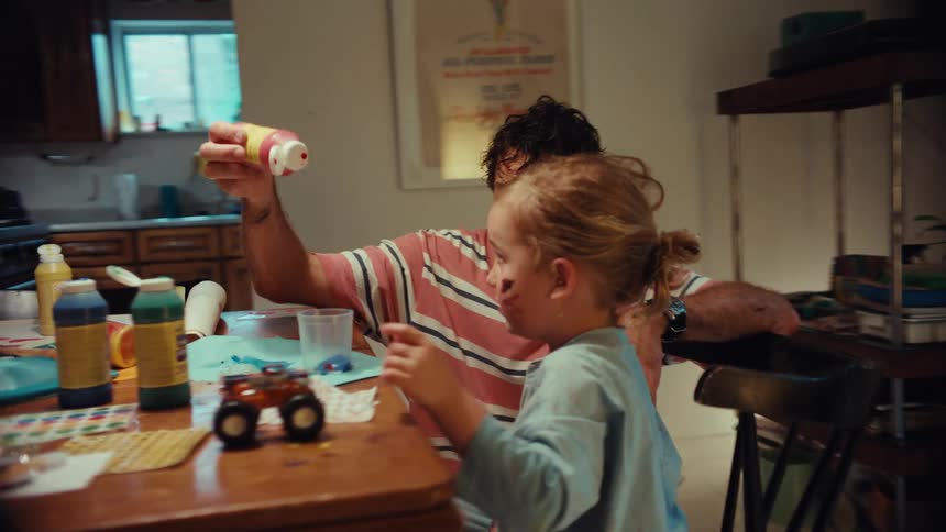 Playful father and child get messy with arts and crafts, squeezing colorful paint at the dining table in their cozy home