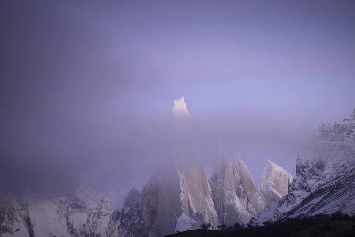 A misty time-lapse reveals the majestic, snow-capped Cerro Torre mountain peaks as the fog clears and the morning sun casts a golden glow