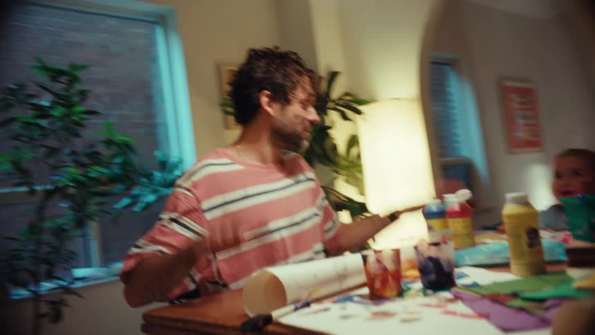 A playful father and his young daughter get messy with paints and crafts at their dining table