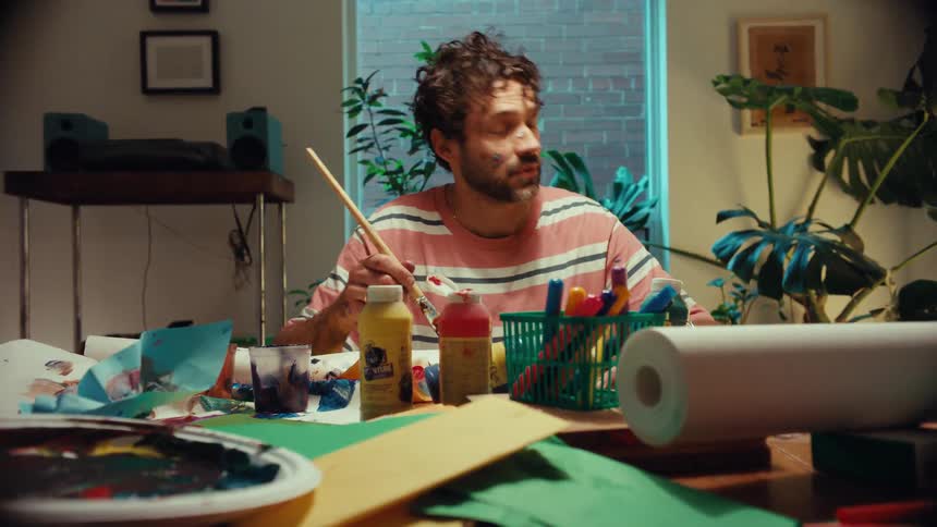 Surprised artist with paint on his face pauses his creative work as a colorful object mysteriously floats by his messy desk