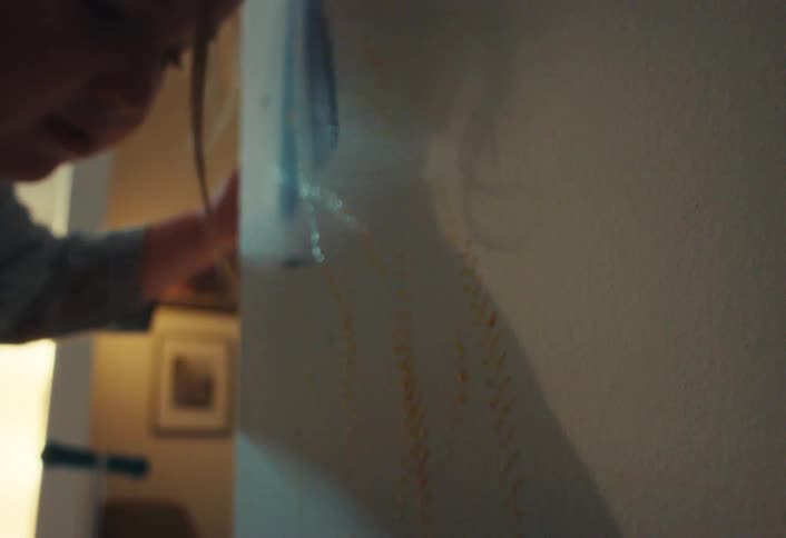 A child drives a toy monster truck with paint on its wheels up a wall, making a colorful mess