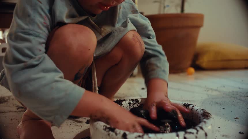 Close-up shot of a messy toddler absorbed in playing with a toy monster truck and a bowl of mud on the floor