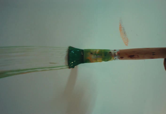 Close-up vertical shot of a paintbrush slowly creating a green stroke on a white canvas