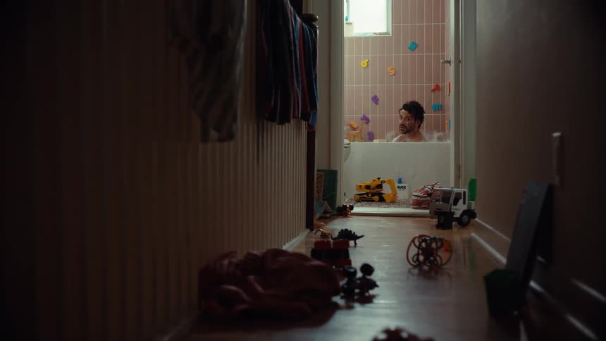 Down a dimly lit hallway cluttered with toys, a tired father tries to find a moment of peace in a bubble bath