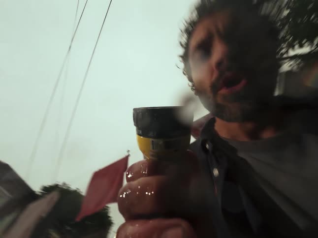 From a low angle point of view, a man washes the camera lens with a garden hose under an overcast sky