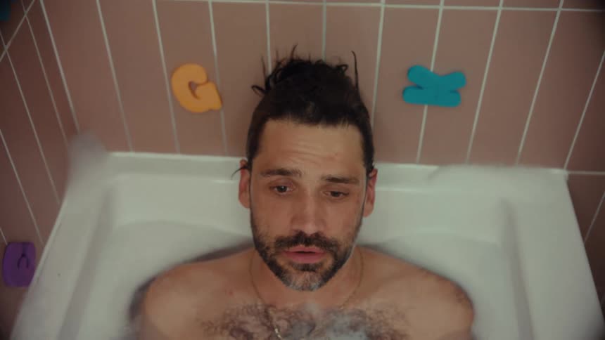 High-angle shot of an exhausted, bearded man sinking back into a bubble bath to find a moment of peace