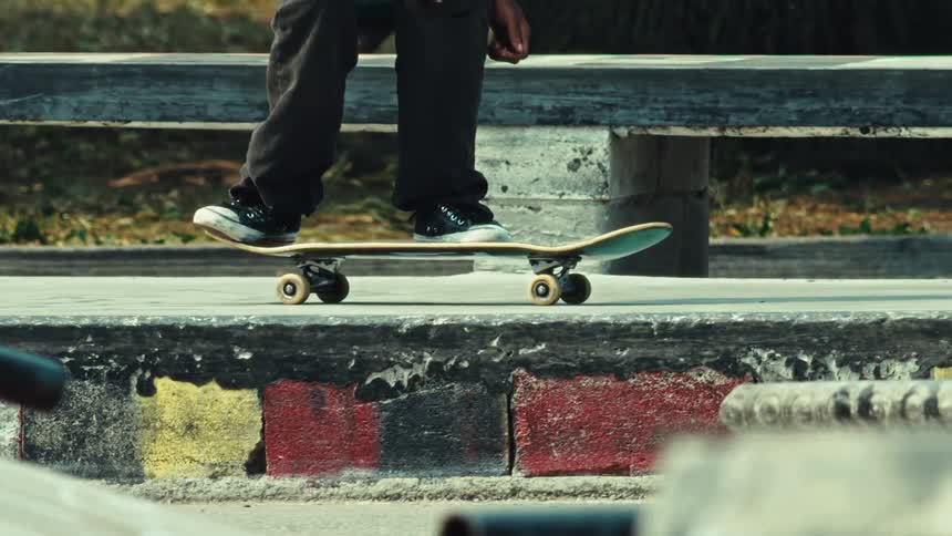 A close-up shot of a skateboarder's shoes and board as they stand still on a concrete ledge in an urban park