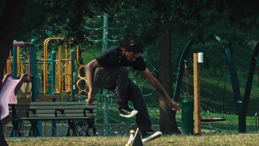 A skateboarder executes a technical grind and flip trick on a rail in super slow motion at a sunny urban park