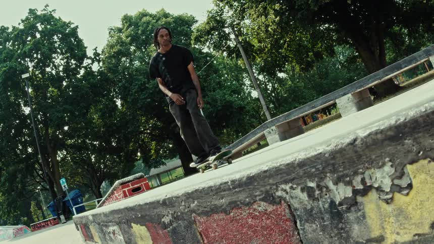 A skateboarder rolls down a concrete ramp in an outdoor skatepark in super slow motion