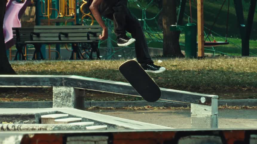 A skateboarder performs a boardslide down a rail in super slow motion at an outdoor skatepark