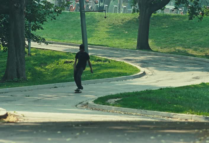 A skateboarder gracefully cruises in slow motion down a winding path through a sunlit park