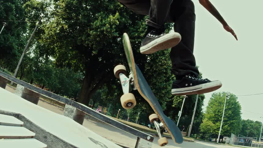 Dynamic slow-motion shot of a skateboarder performing a flip trick over a stair set at a sunny outdoor skatepark