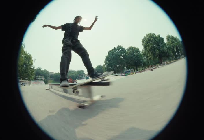Fisheye lens follows a skateboarder in slow motion as they perform a boardslide trick on a rail and fall off in a sunny skatepark