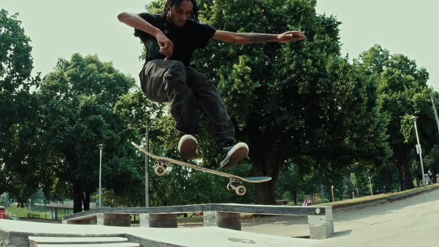 A skateboarder executes a perfect kickflip down a set of stairs at the skatepark in super slow motion