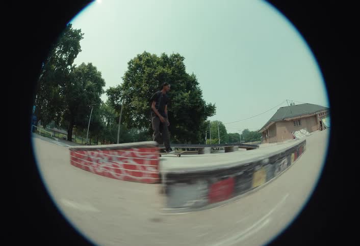 Slow motion fisheye shot of a skateboarder bailing a kickflip trick off a ledge in a sunny urban skatepark