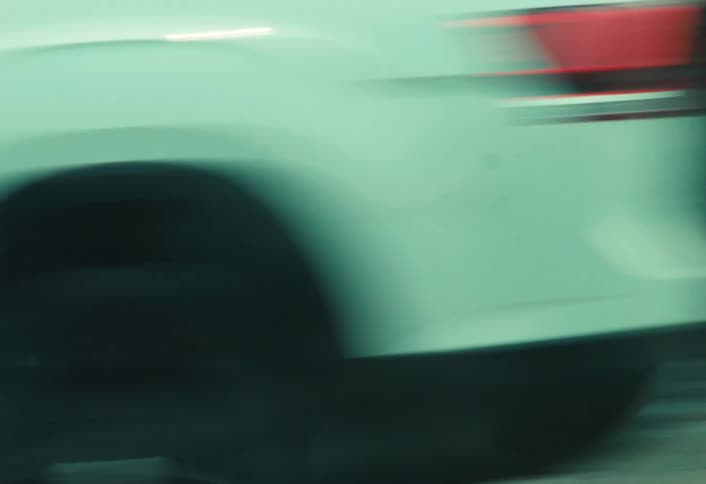 A low-angle tracking shot follows a person skateboarding down a gritty city sidewalk as traffic blurs past