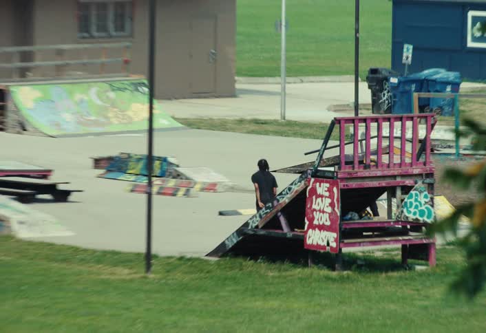 A long shot zooms out from a skateboarder practicing tricks alone at a graffiti-filled skatepark