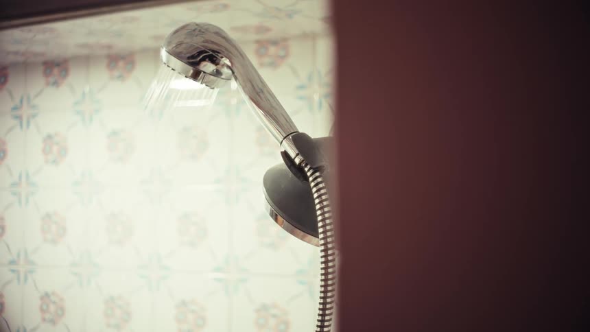 Water runs from a modern chrome shower head in a bathroom with decorative tiles