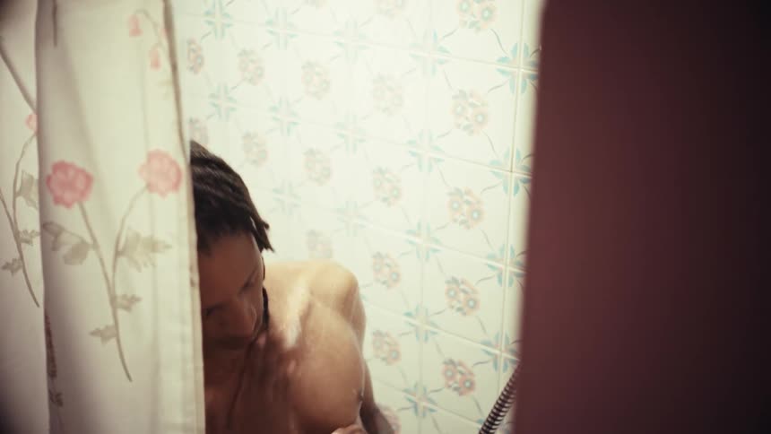 A young man with dreadlocks enjoys a warm shower, seen from behind the curtain in a vintage-tiled bathroom