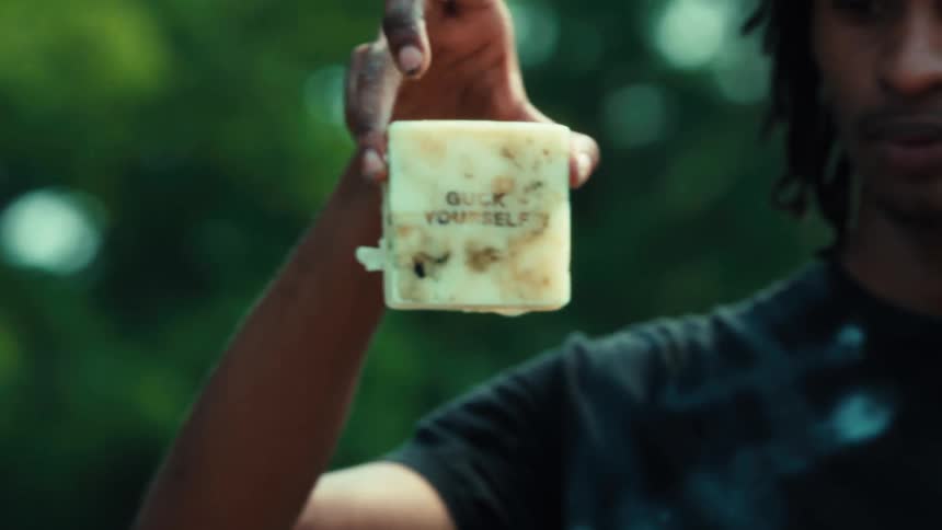 A man holds up a handmade bar of soap with the defiant message 'Guck Yourself' stamped on it
