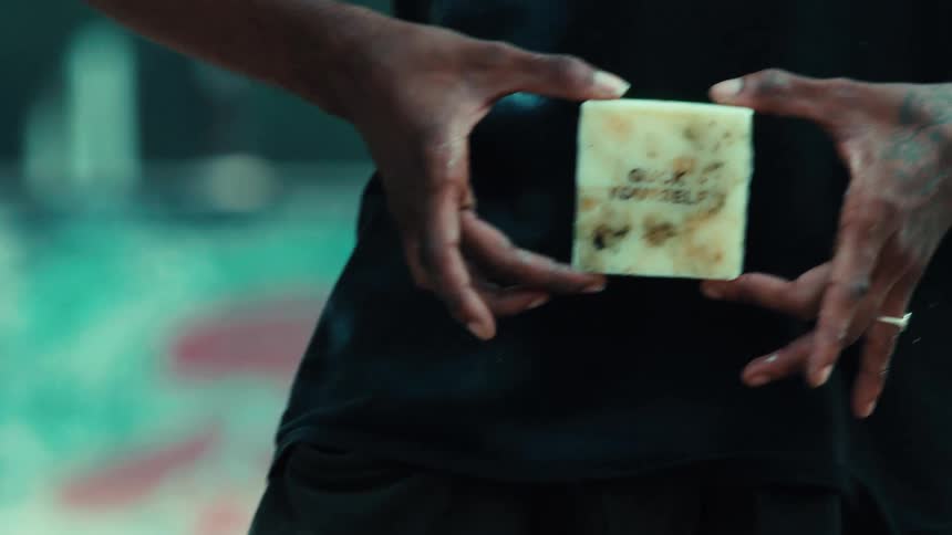 A skateboarder reveals a bar of 'Guck Yourself' wax in an urban setting