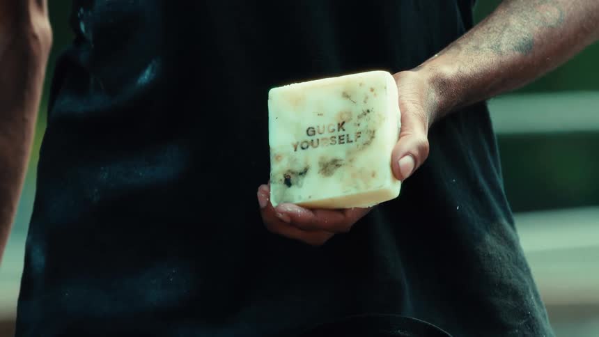 Close-up of a tattooed arm holding a block of skate wax with text on it