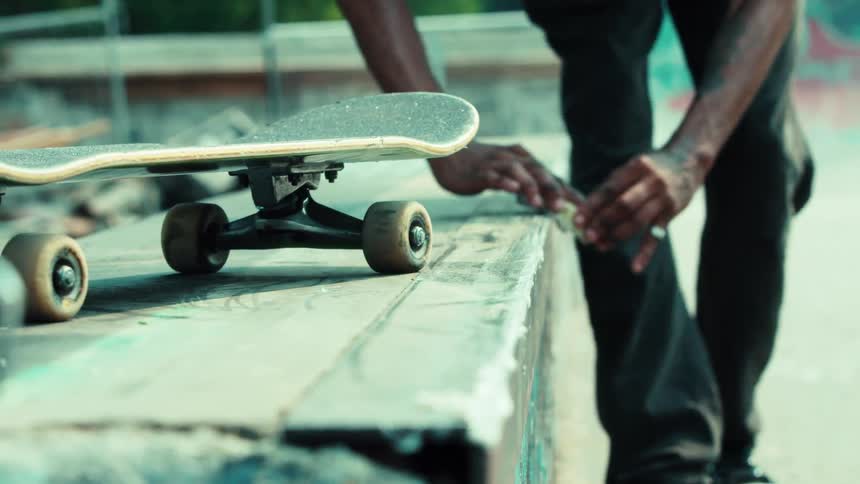 Close up slow motion shot of a skateboarder waxing a concrete ledge at an urban skatepark