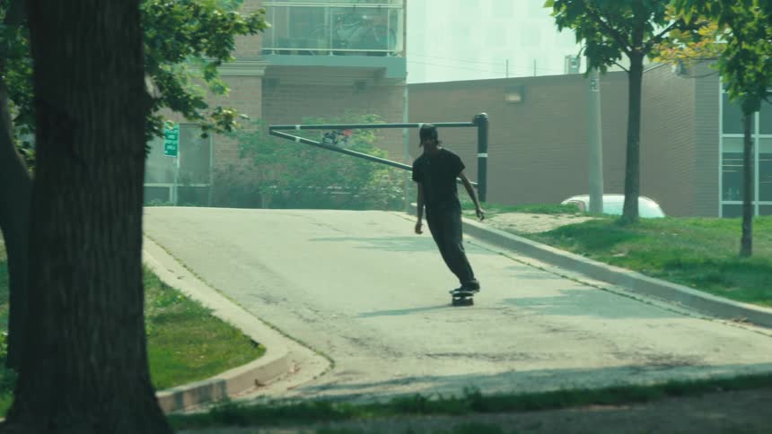 Slow motion long shot of a young man skateboarding down a paved hill in a suburban neighborhood