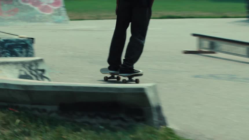 A close-up tracking shot follows a skateboarder's legs and board as they glide through a concrete skatepark