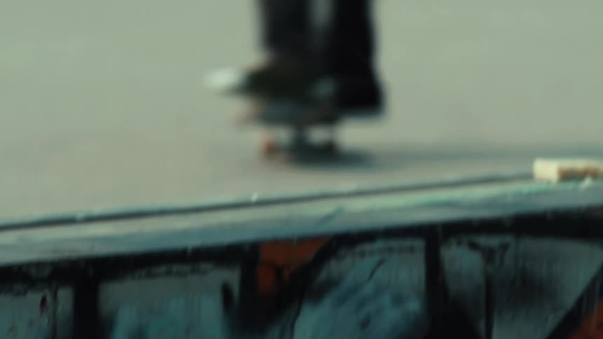 A close-up shot following a skateboarder's feet as they grind on a rail and ride up a graffiti-covered ramp in a skatepark