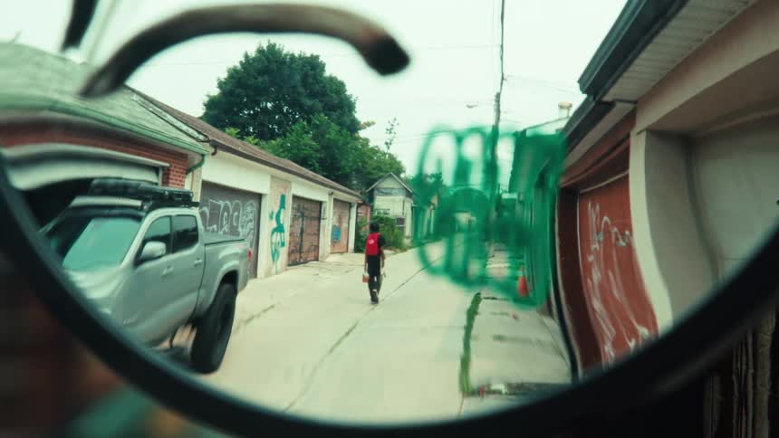 A point-of-view shot through sunglasses of a person with a red backpack walking down a graffiti-covered urban alley