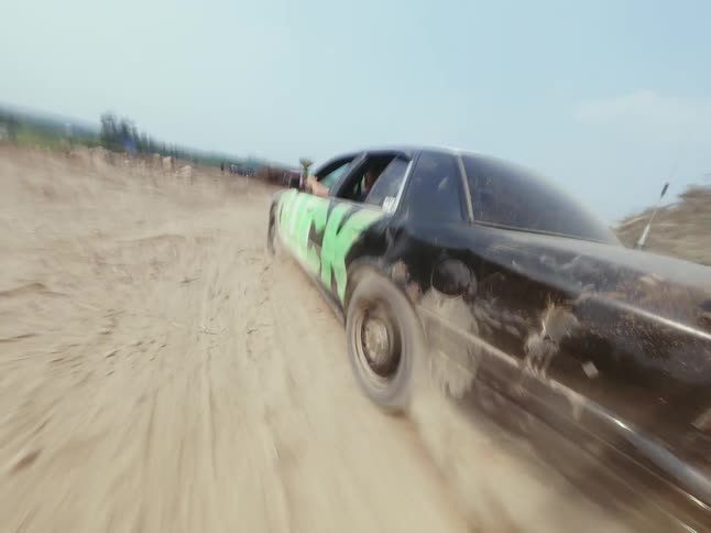 A point-of-view shot from a speeding car kicking up dust on a dirt road as a person aims a paintball gun out the window