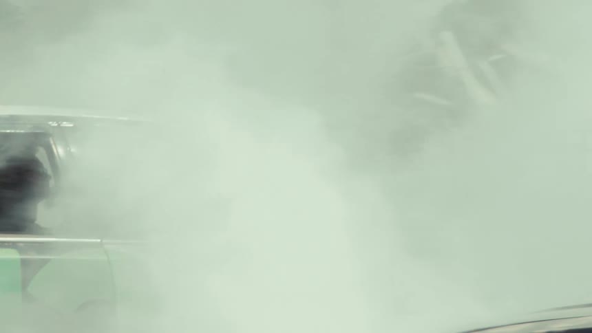 A souped-up demolition derby car speeds along a dirt track before it's engulfed in a cloud of thick white engine smoke