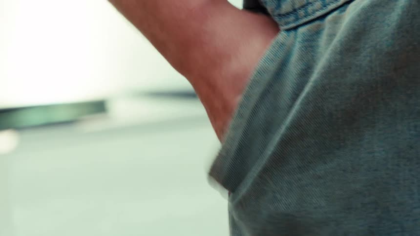 A close-up in slow motion shows a worker's hand putting keys into the pocket of their denim jeans