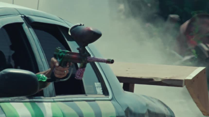 A paintball gun fires out of a car window in super slow motion, with smoke billowing in the background