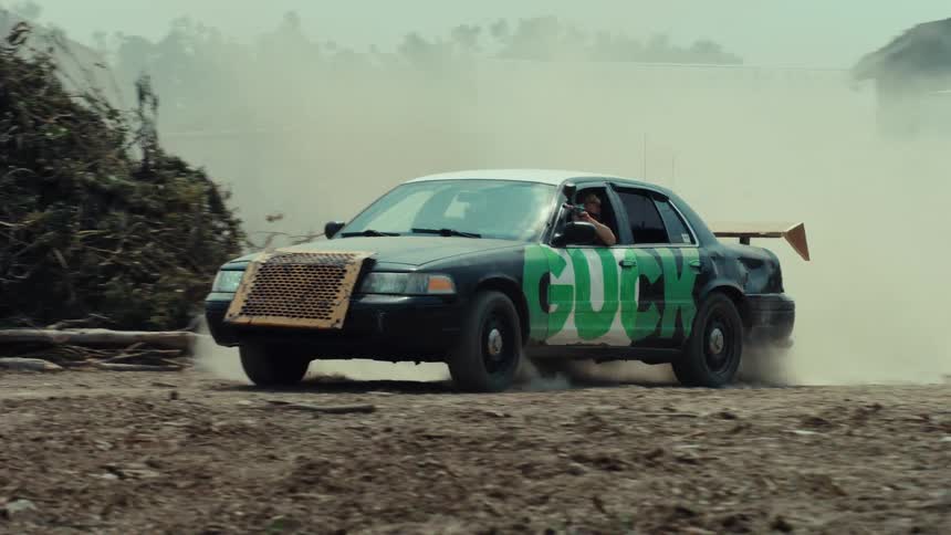 A custom black and white sedan drifts in slow motion on a dirt road, kicking up a large cloud of dust