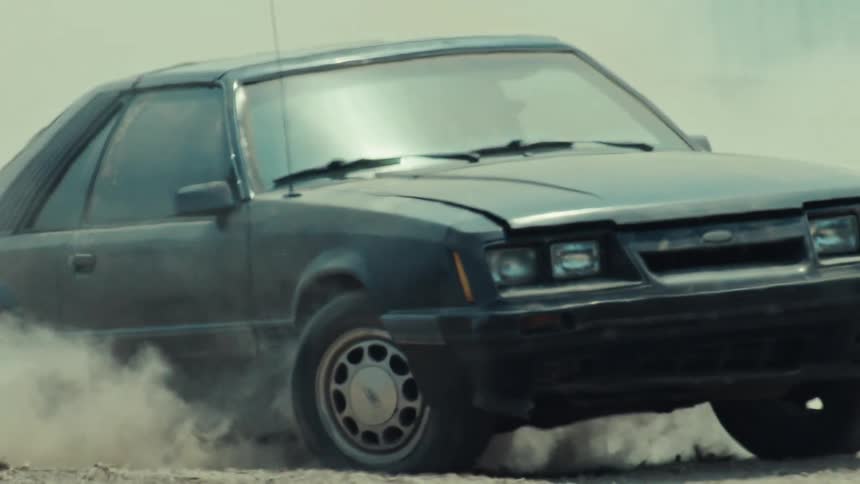 Close-up of a classic black American muscle car spinning its tires and creating a massive cloud of dust in slow motion