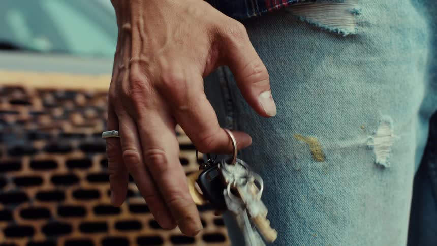 Slow motion close-up of a man's hand anxiously spinning a keychain on his finger next to his worn blue jeans