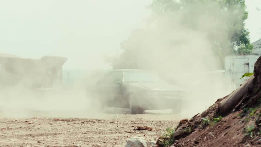 Two cars engage in an intense chase through a dusty wasteland as a man aims a paintball gun from the passenger window