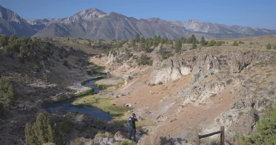 Crane shot reveals a hiker photographing a beautiful river valley with the majestic Sierra Nevada mountains in the background